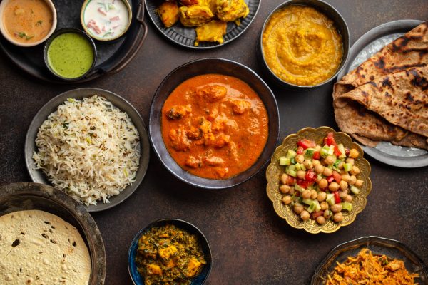 Authentic Indian dishes and snacks Variety of Indian food, different dishes and snacks on dark rustic background. Pilaf, butter chicken curry, rice, palak paneer, chicken tikka, dal soup, naan bread, assortment of chutney. Top view